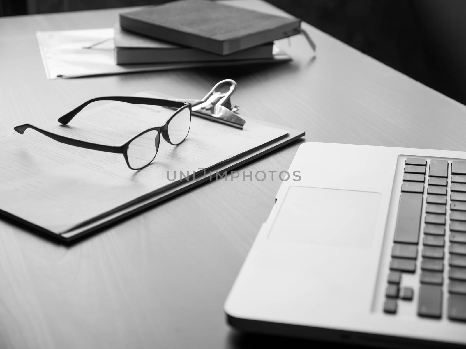 Office desk with laptop, glasses, documents and book. Black and White tone