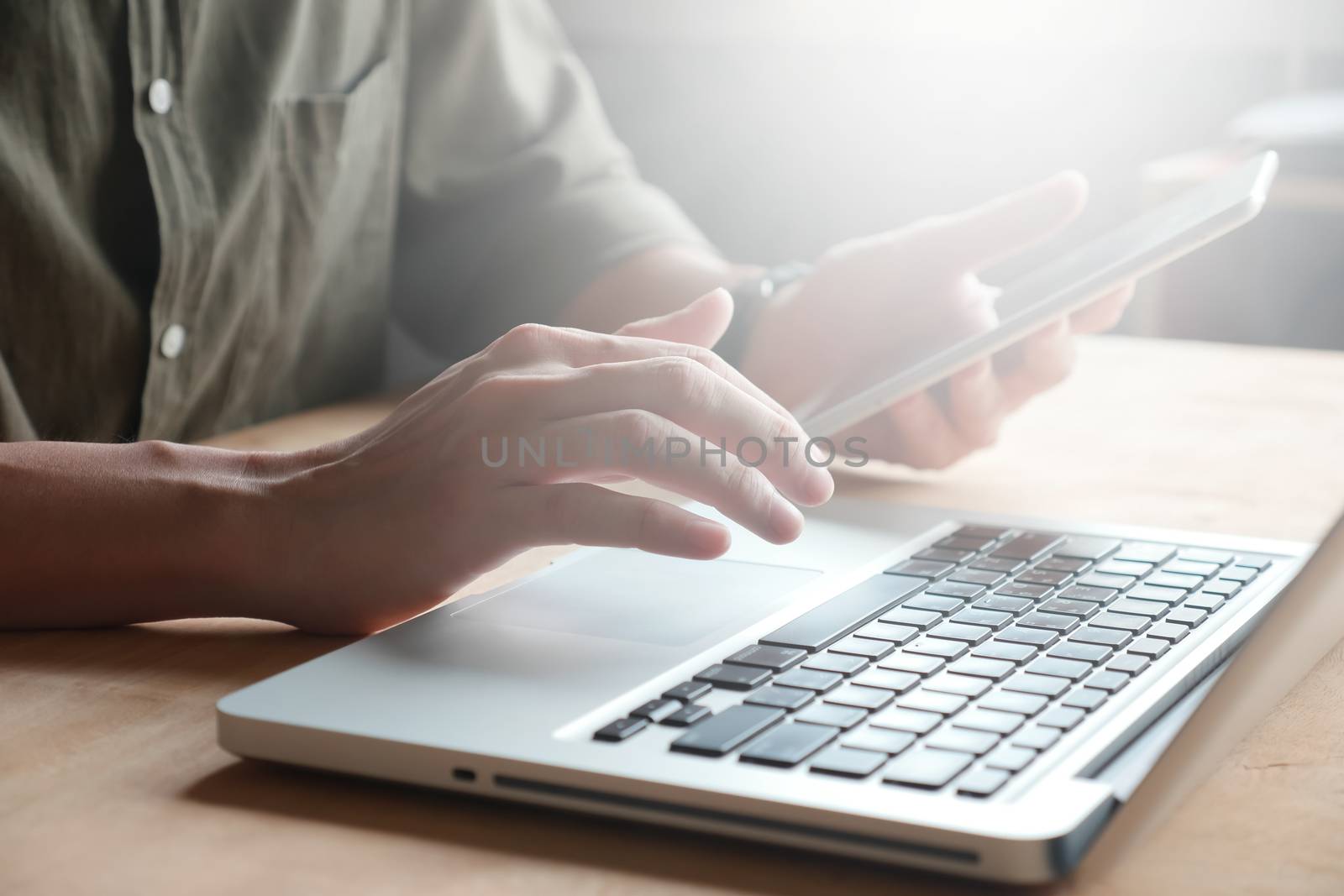 Close up of Male hands using laptop and tablet on the table, toned with sunlight