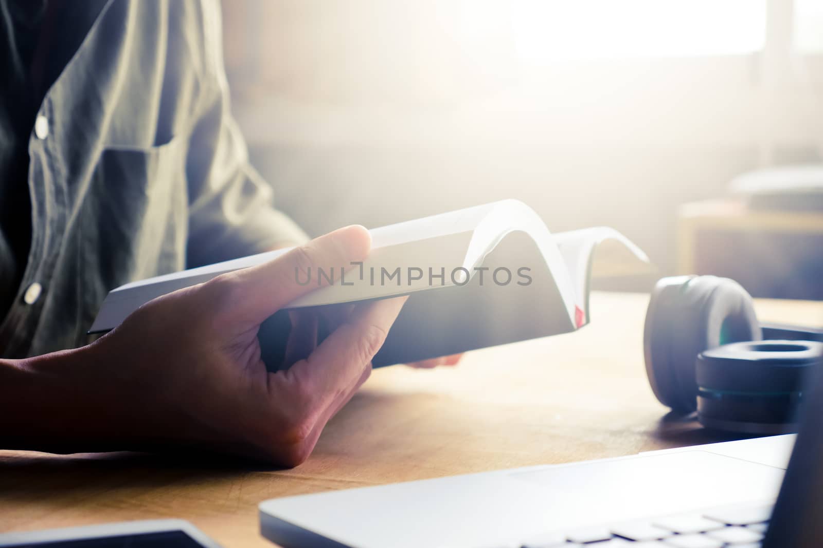 Close up of casual man reading a book on the desk at home, toned with sunlight