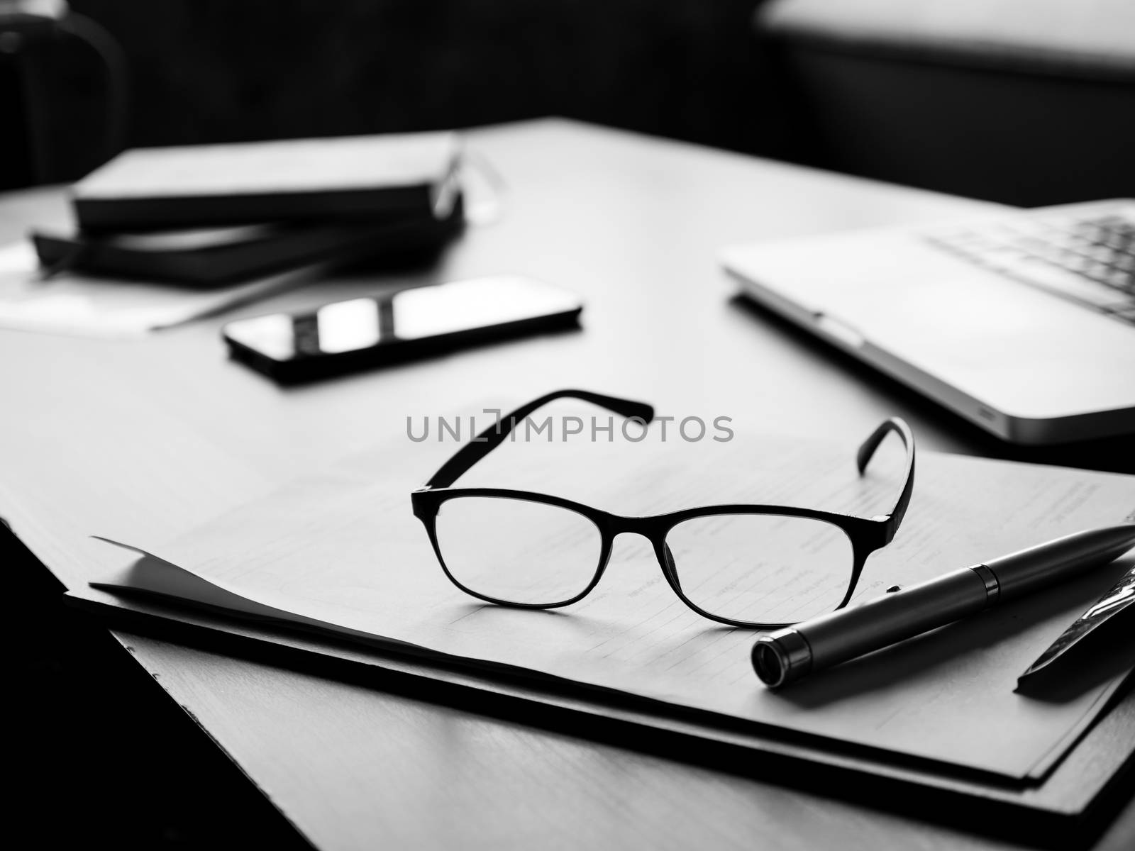 Office desk with glasses, documents,laptop,smart phone and notebook. Black and White tone