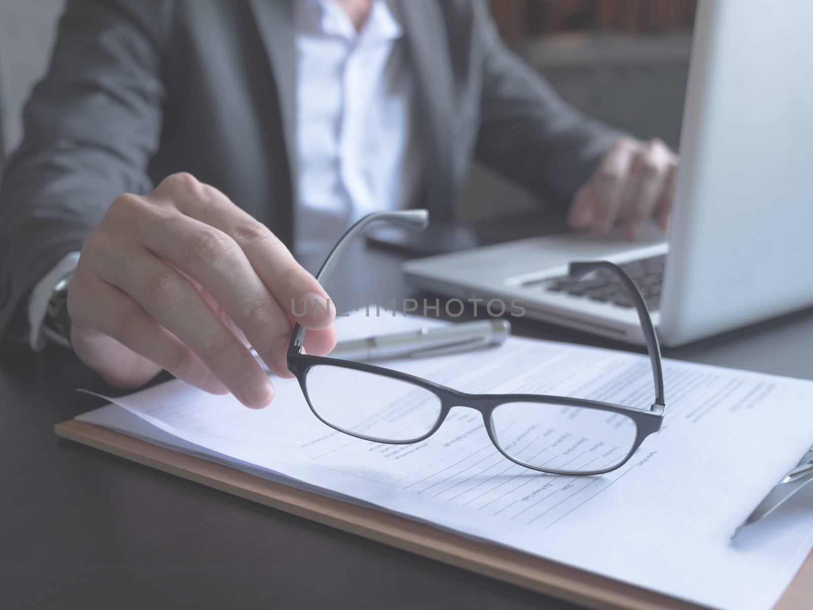 Close up of Businessman holding eyeglasses, he is using laptop and reading documents on the office desk.