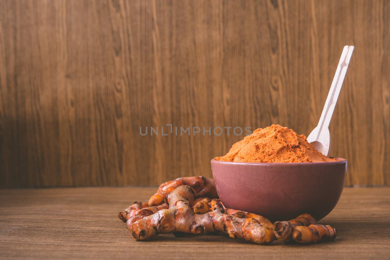 Turmeric roots with turmeric powder on wooden background.