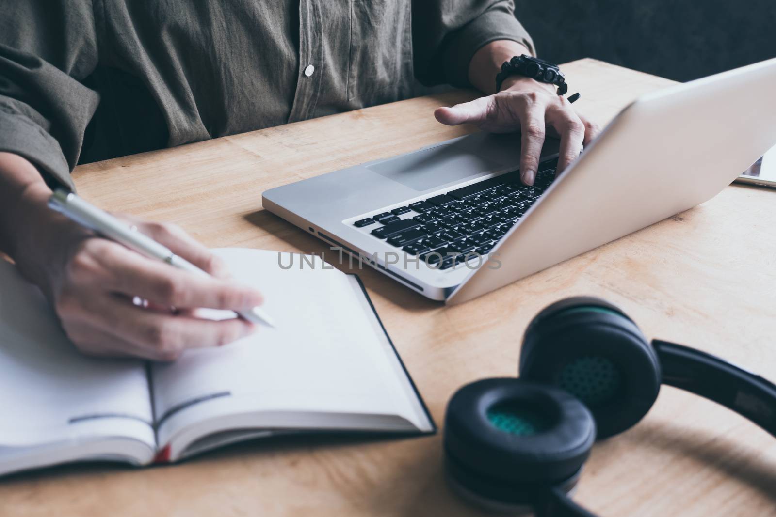 Close up of casual man writing note and using laptop on the desk.