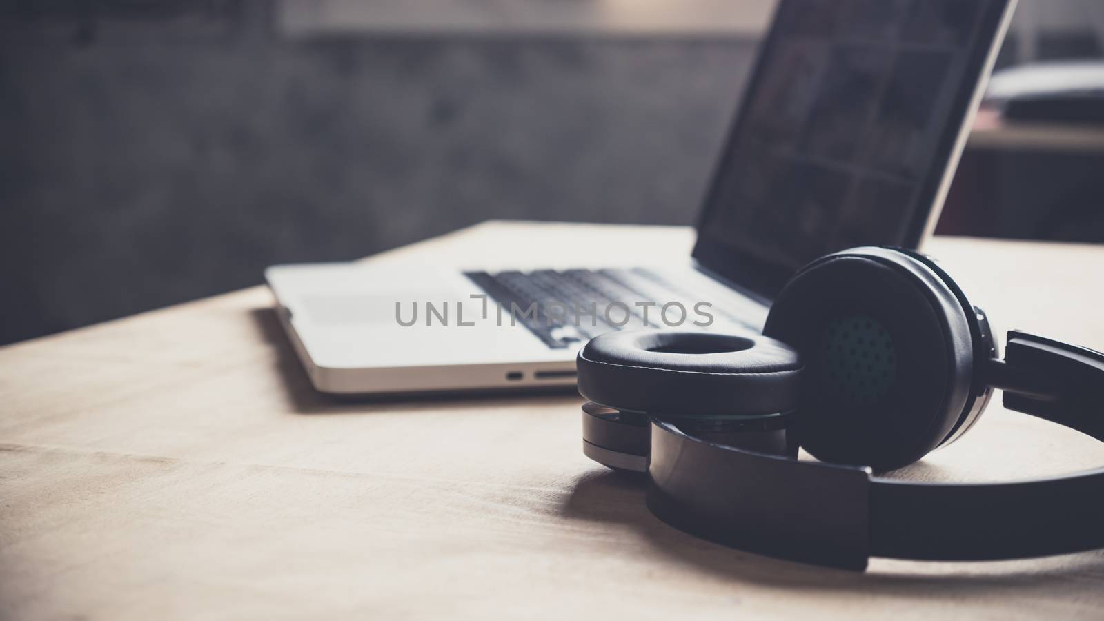 Laptop and headphone on wooden table at home.