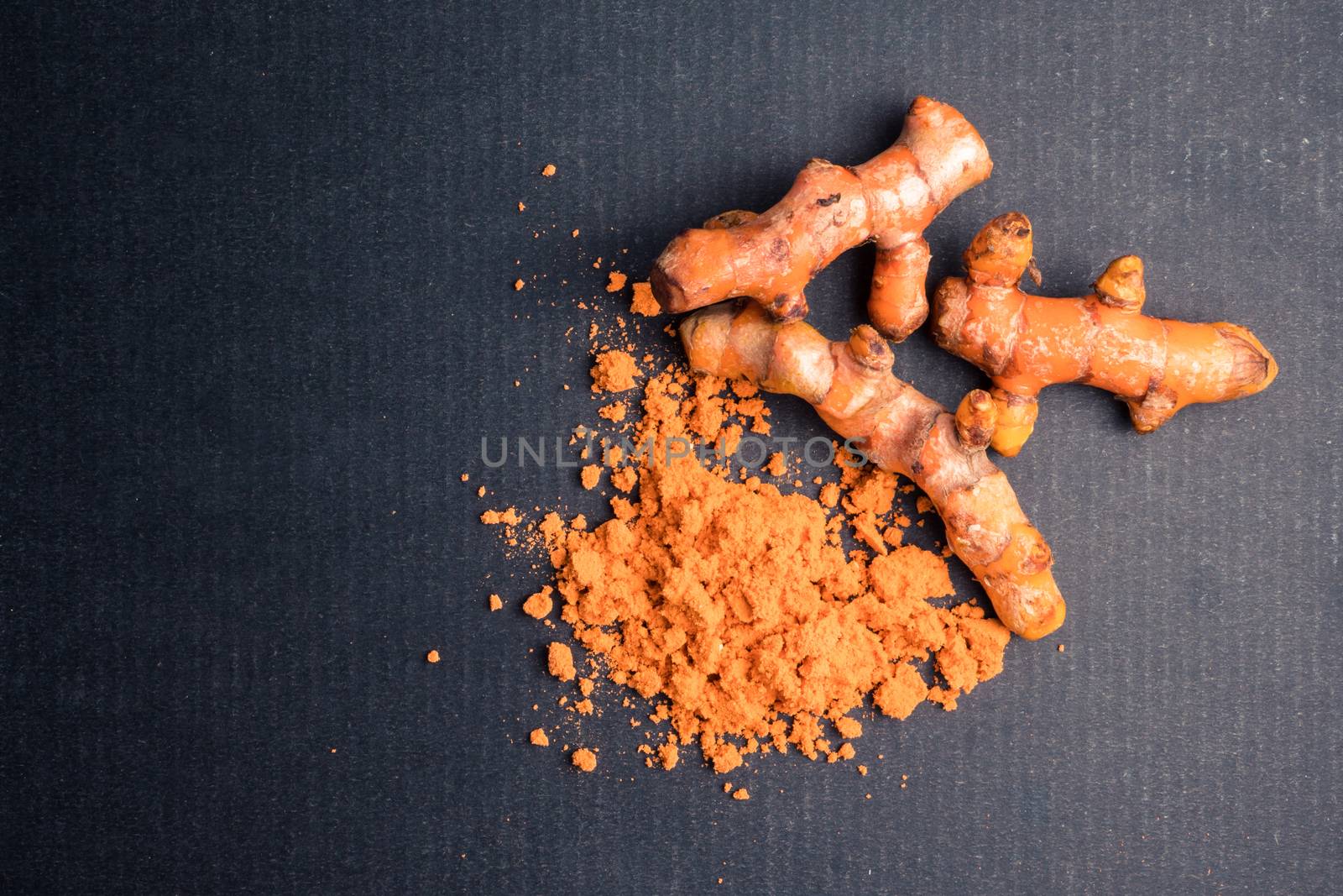 Turmeric roots with turmeric powder on black background.