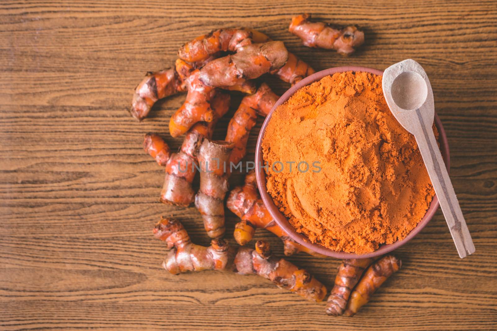Turmeric roots with turmeric powder on wooden background.