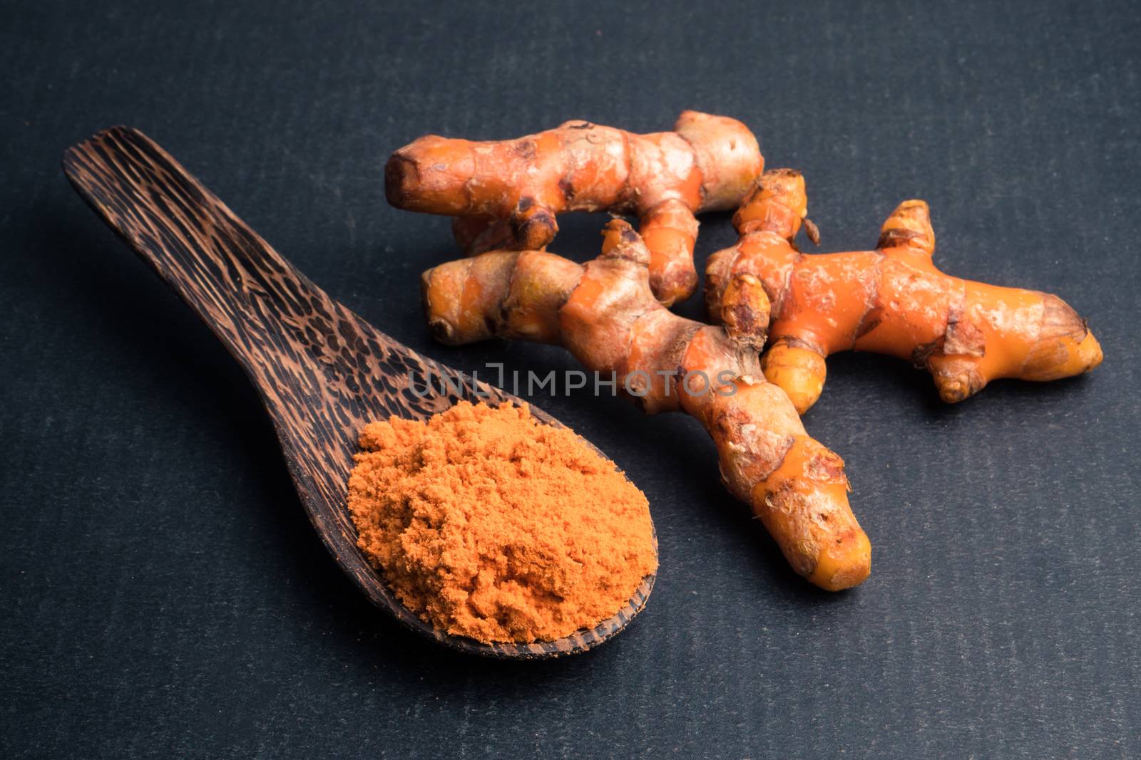 Turmeric roots with turmeric powder on black background.