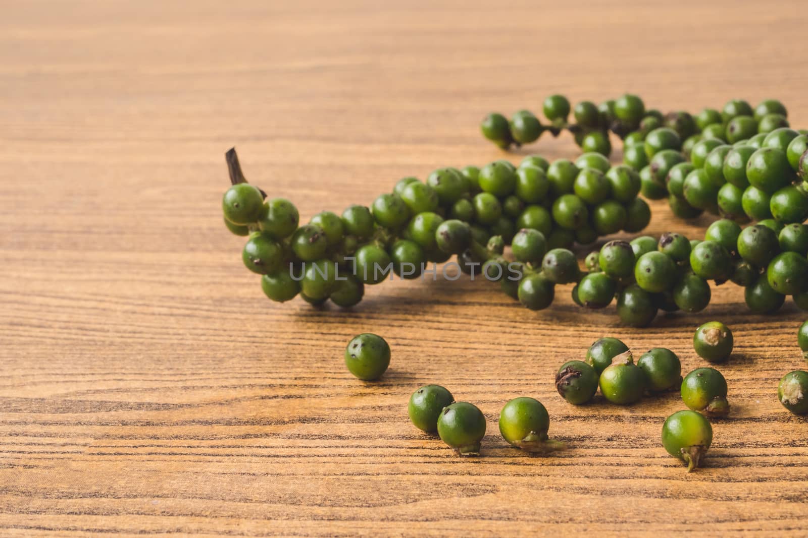 Green peppercorns on wooden background.