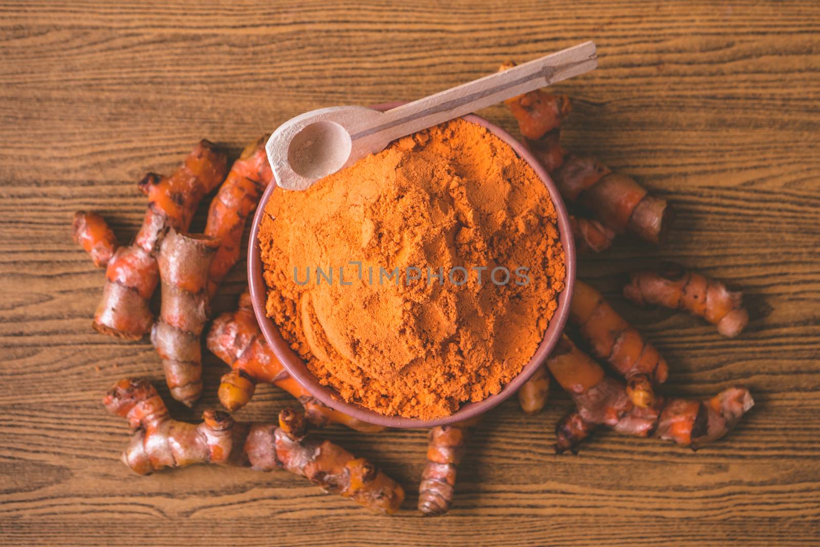 Turmeric roots with turmeric powder on wooden background.