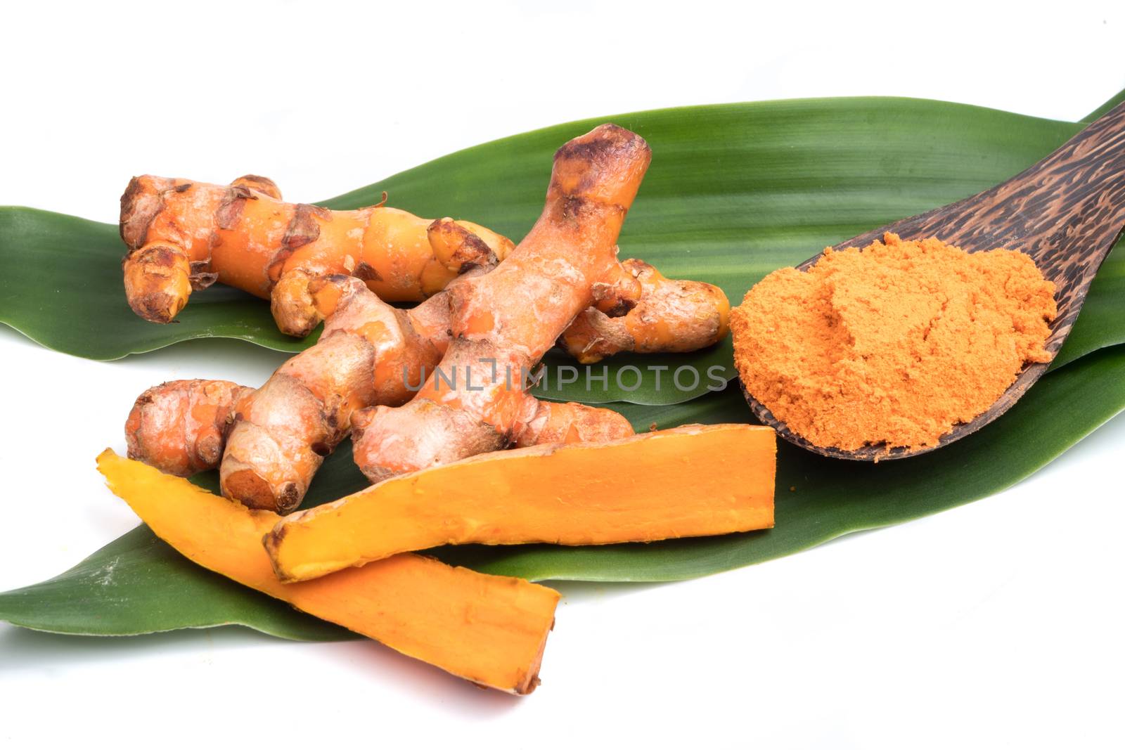 Turmeric roots with turmeric powder on green leaf over white background.
