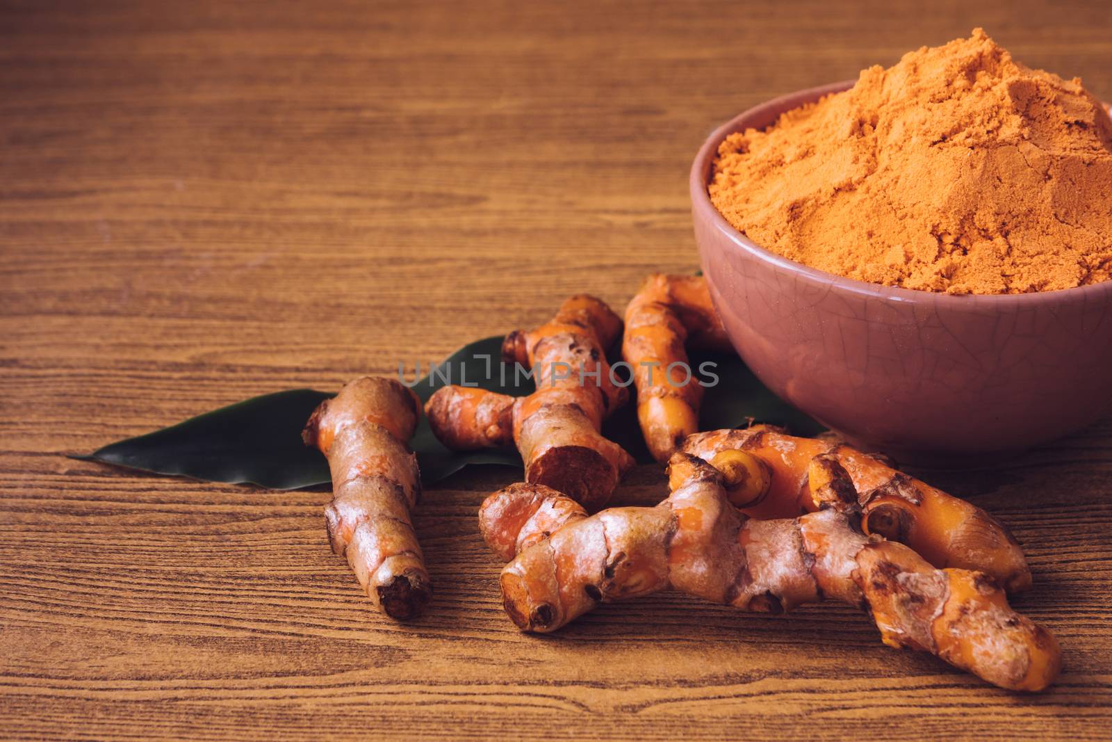 Turmeric roots with turmeric powder on wooden background.