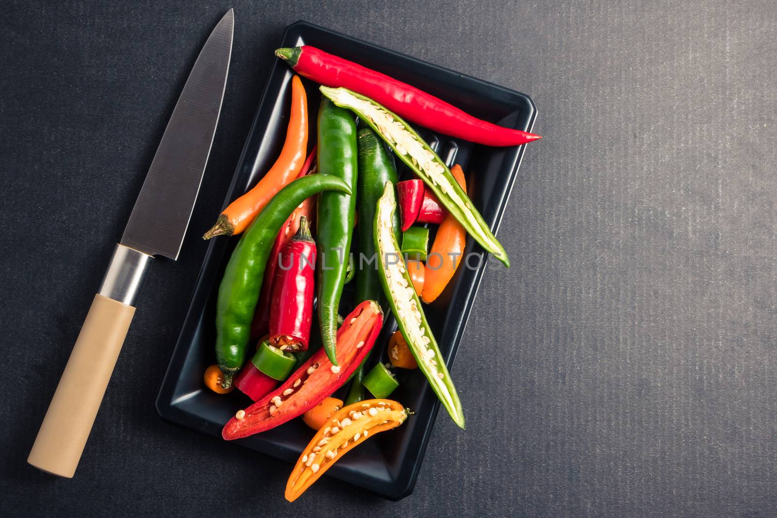 Colorful mix of chili pappers with knife on  black background. Free space for text