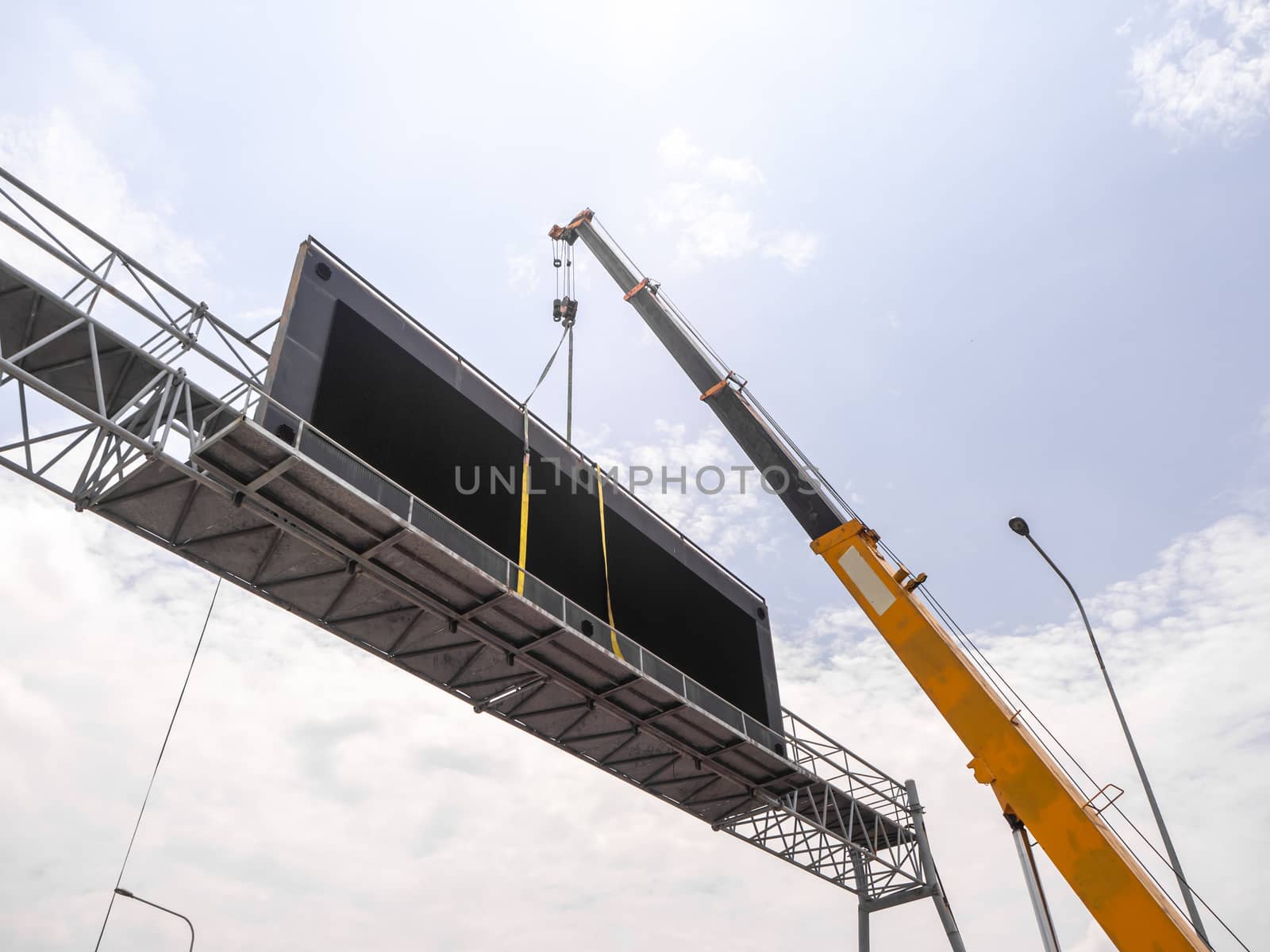Construction site crane is lifting a led signboard for advertise by shutterbird