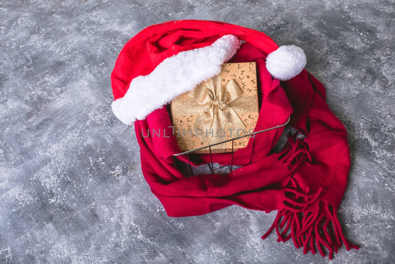 Top view of santa hat with scarf and gift box on gray grunge background.