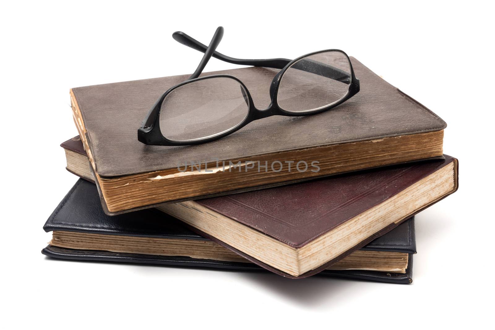 A stack of old books with eyeglasses on a white background. by ronnarong