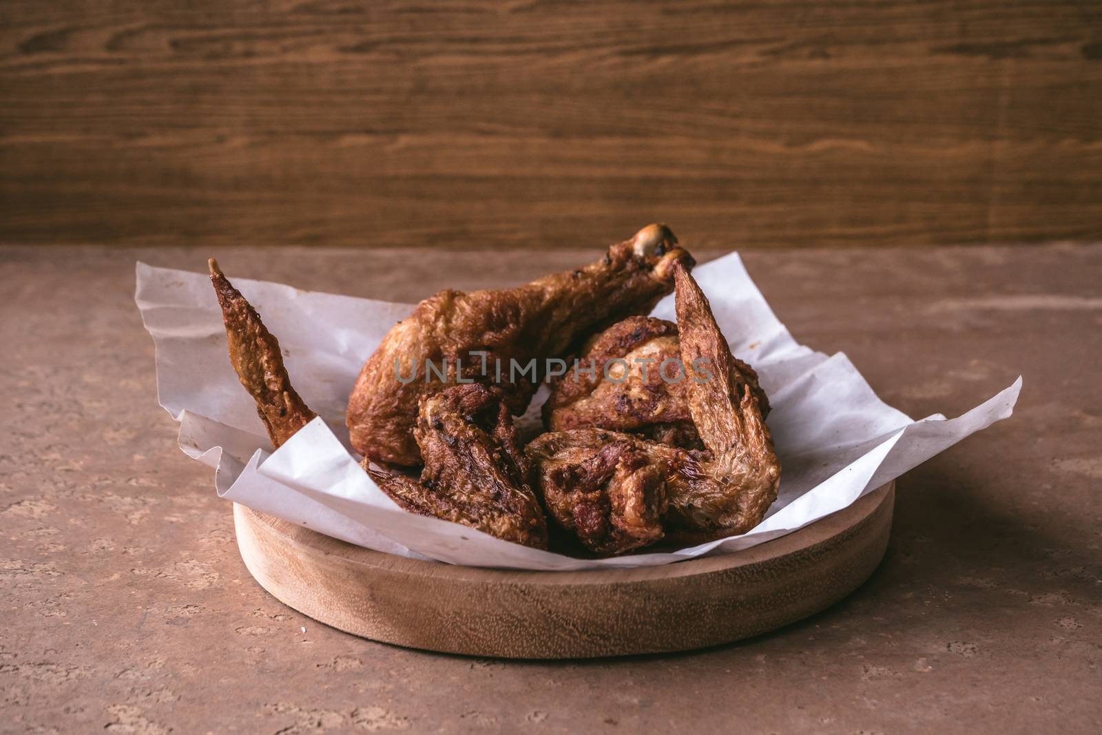 Fried chicken legs and wings in wooden dish on the table.
