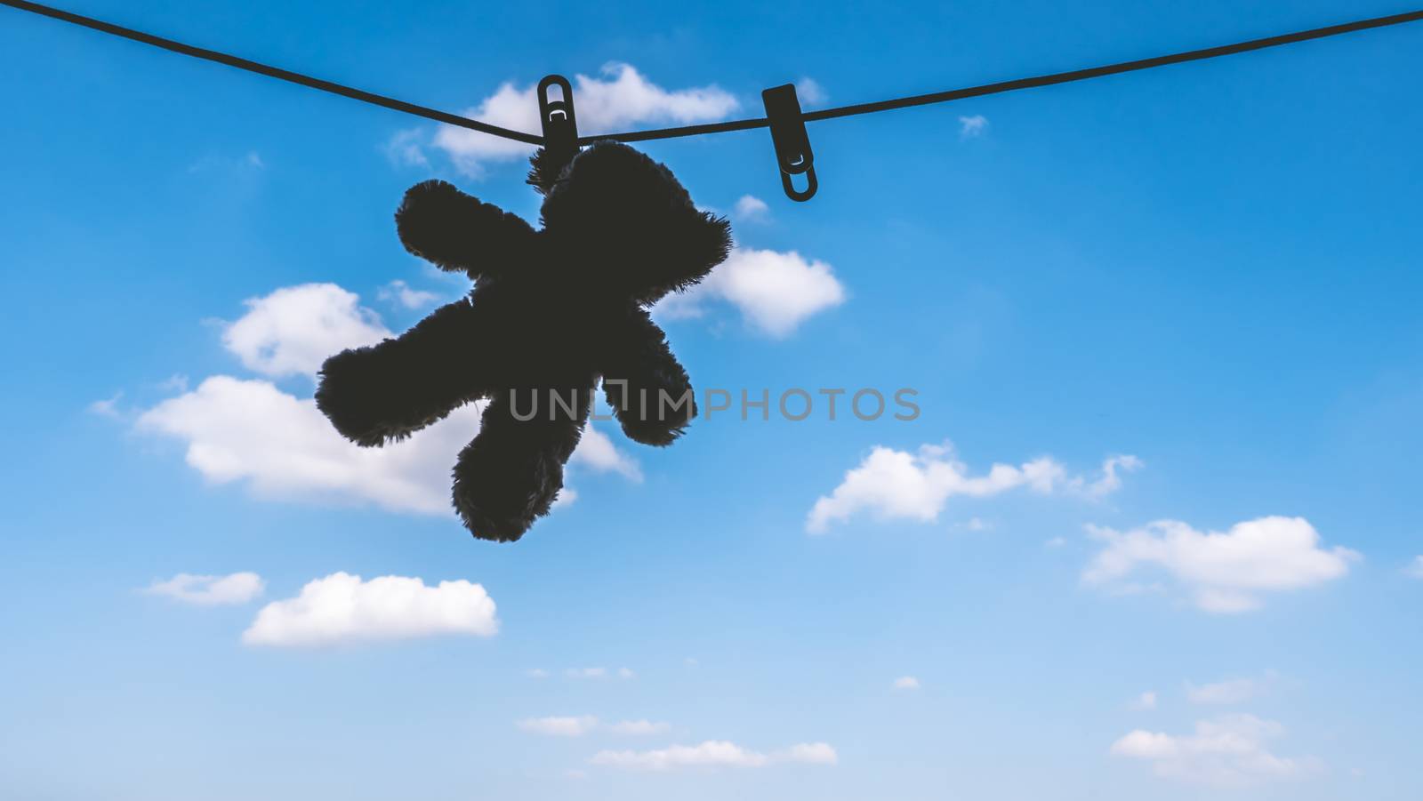 Silhouette of Teddy bear hanging on the clothes line with blue sky.