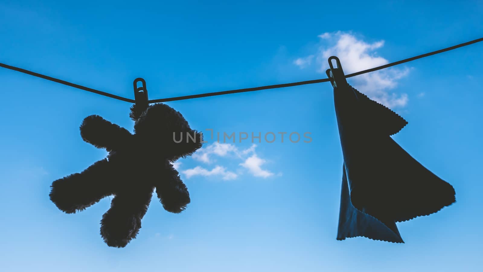 Silhouette of Teddy bear and napkin hanging on the clothes line with blue sky.