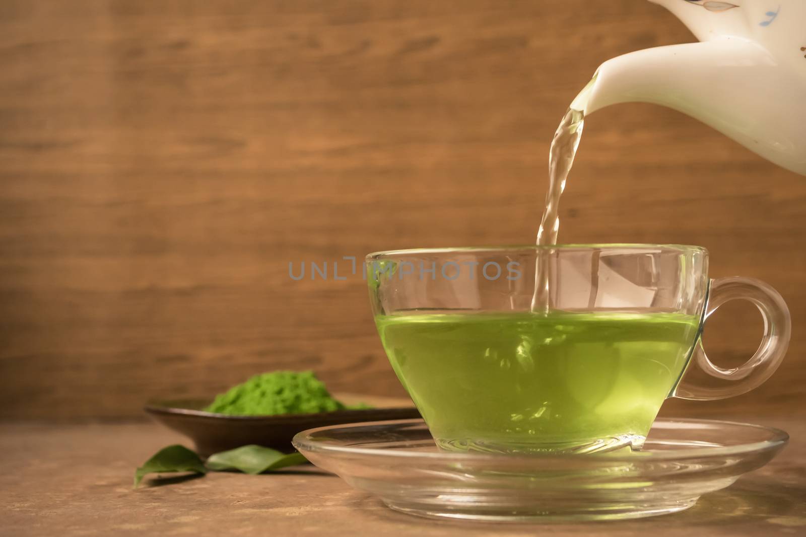 Green tea being poured into glass tea cup on the table by ronnarong