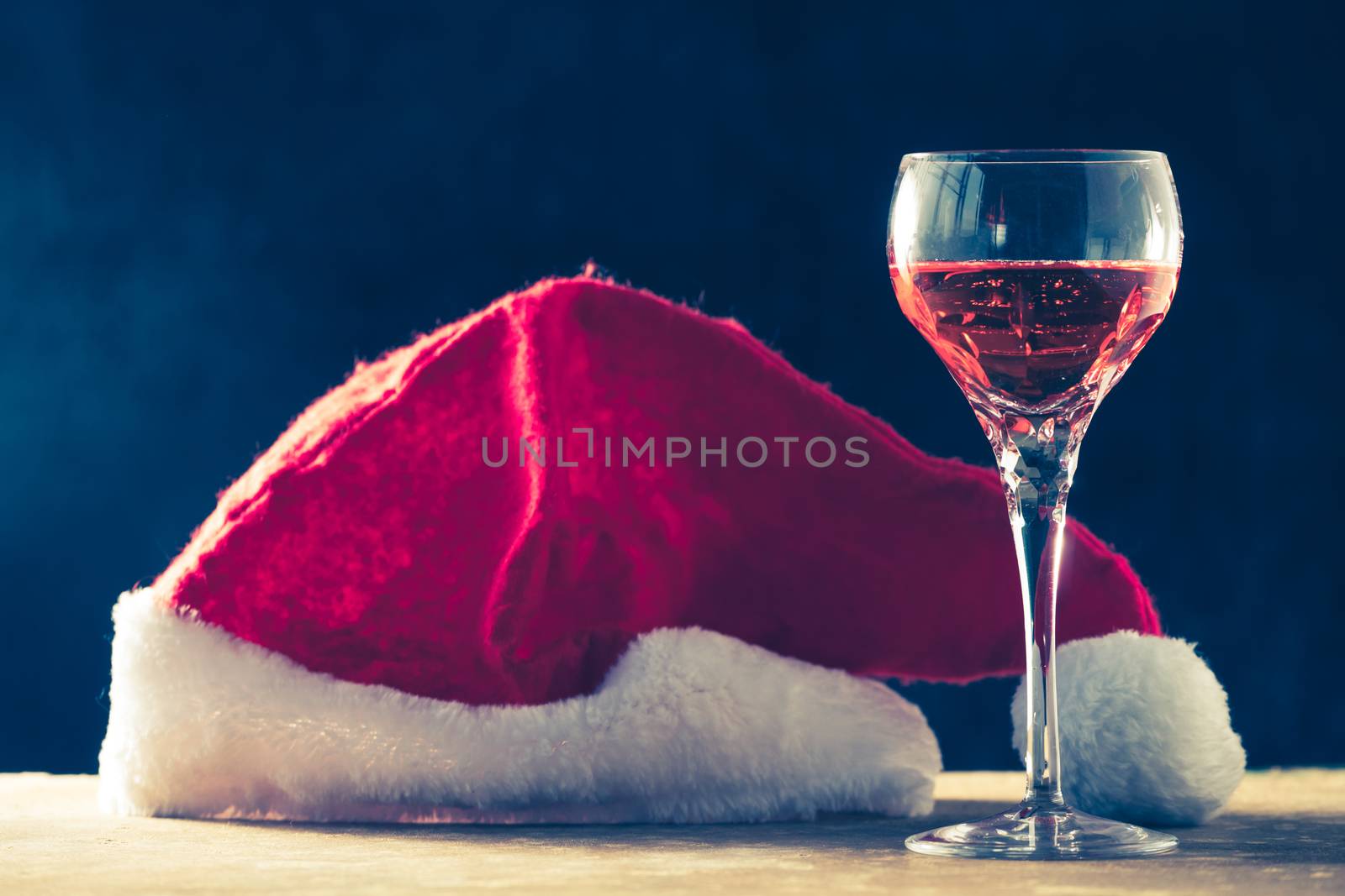 Glass of wine with Santa hat on the wooden table, black background by ronnarong