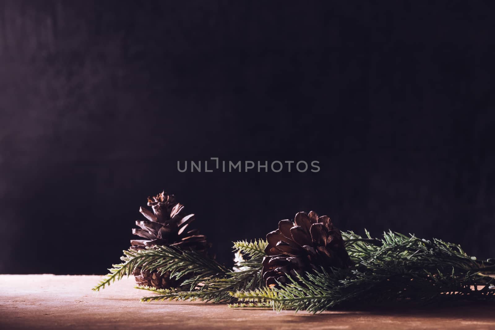 Pine cones with branches on the wooden table, black background, free space for text