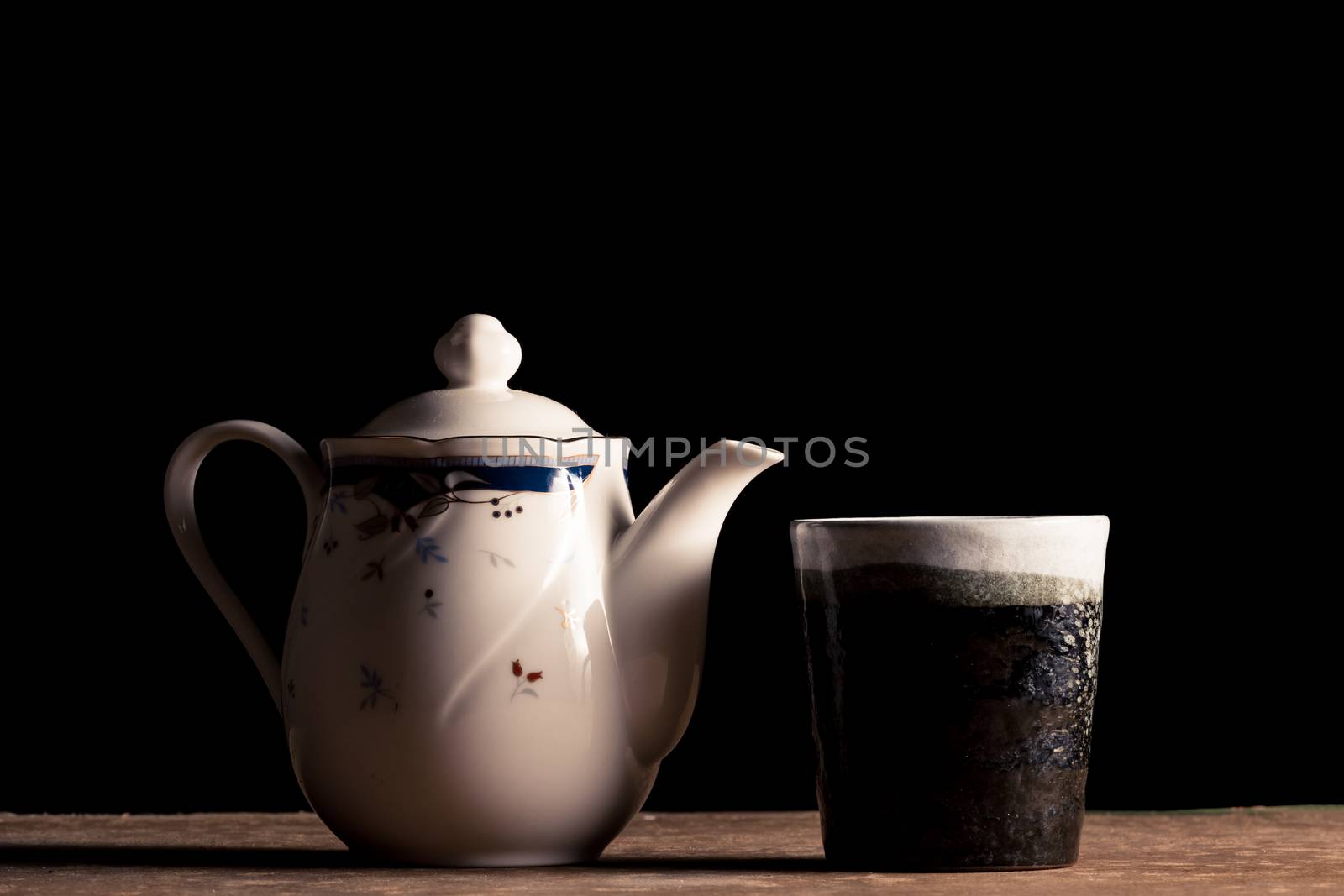 Ceramic Tea pot and tea cup on the table, Black background. by ronnarong