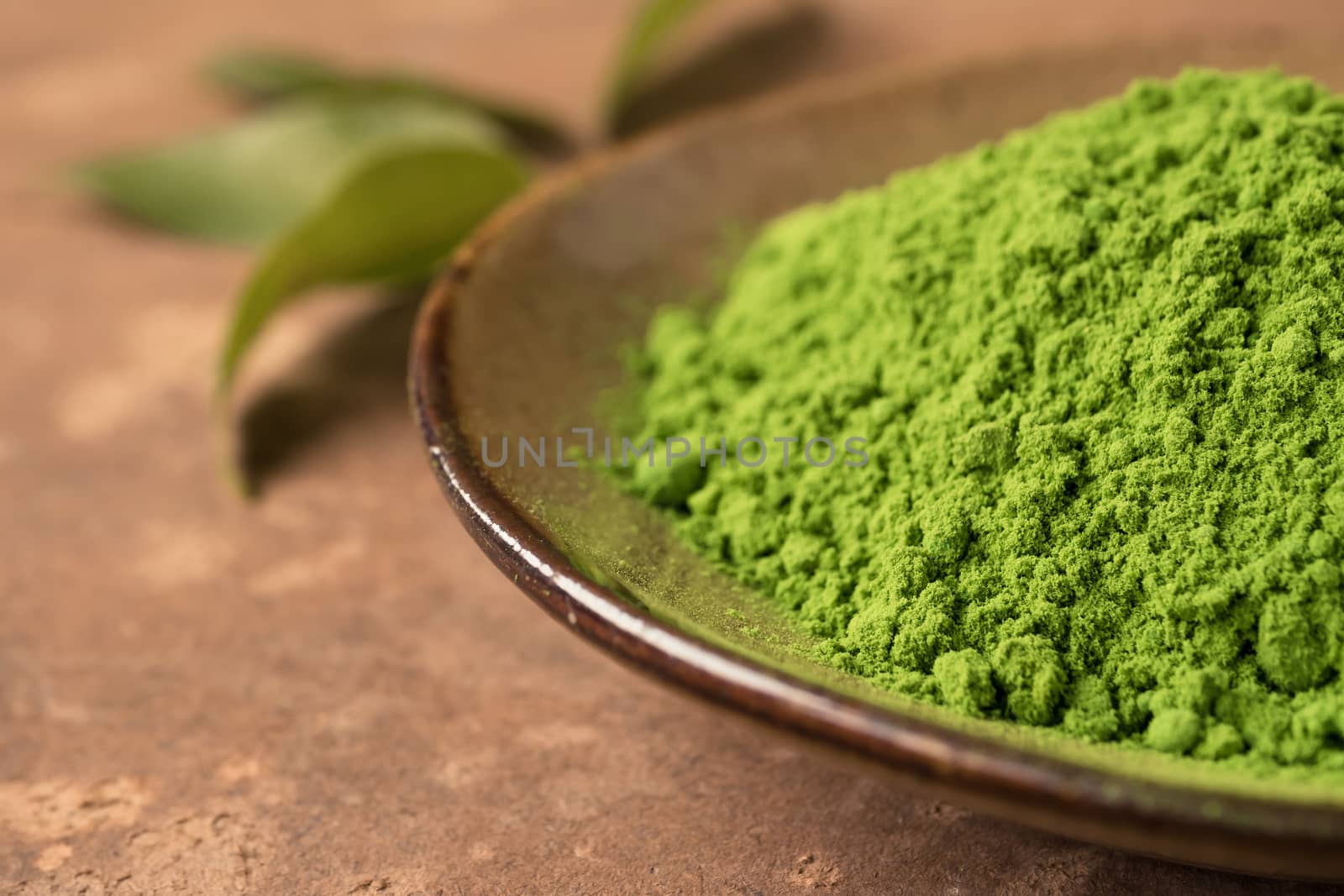 Close up of green tea powder in ceramic dish with leaf on the table.