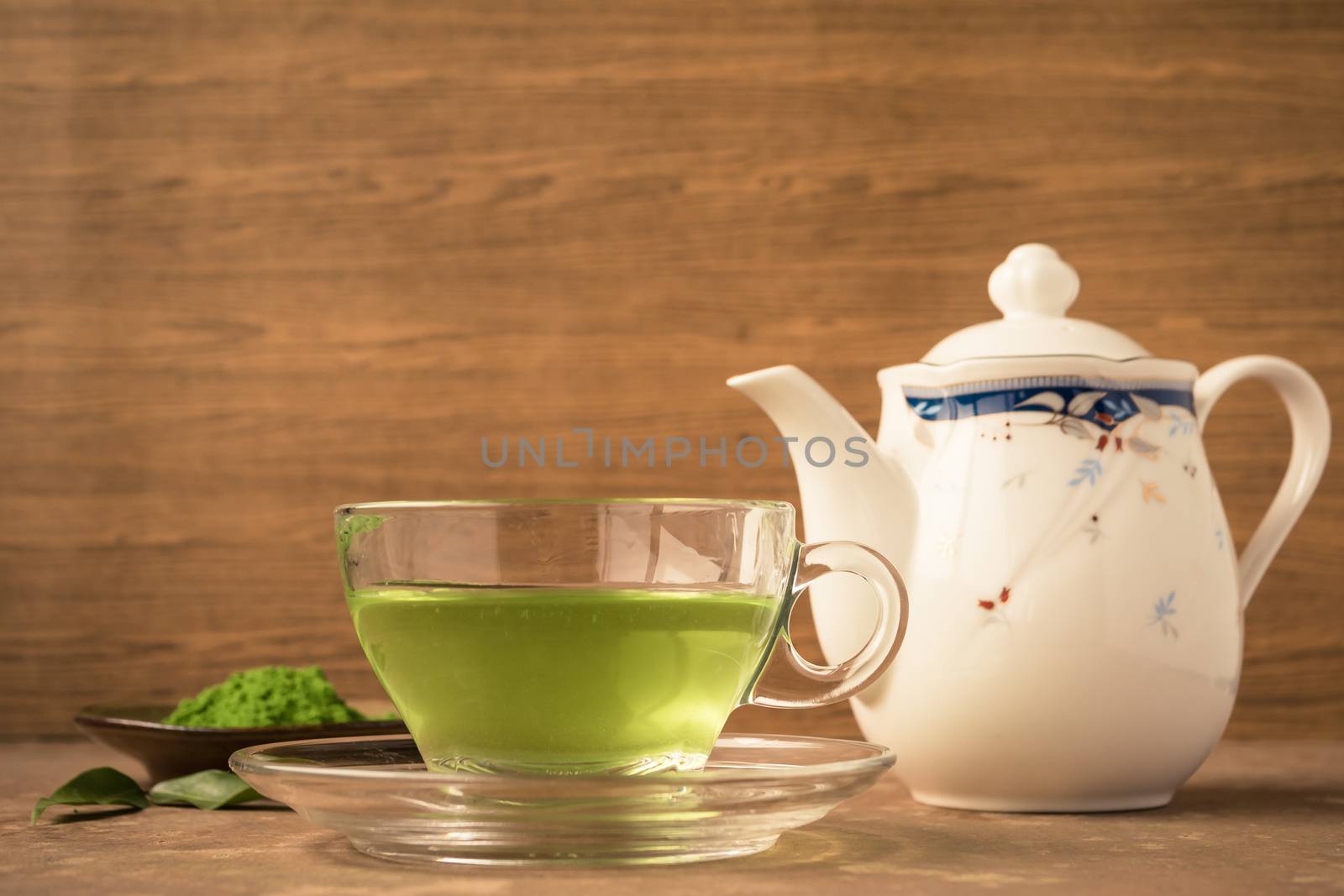 Glass cup of hot tea with green tea powder and teapot on the table.