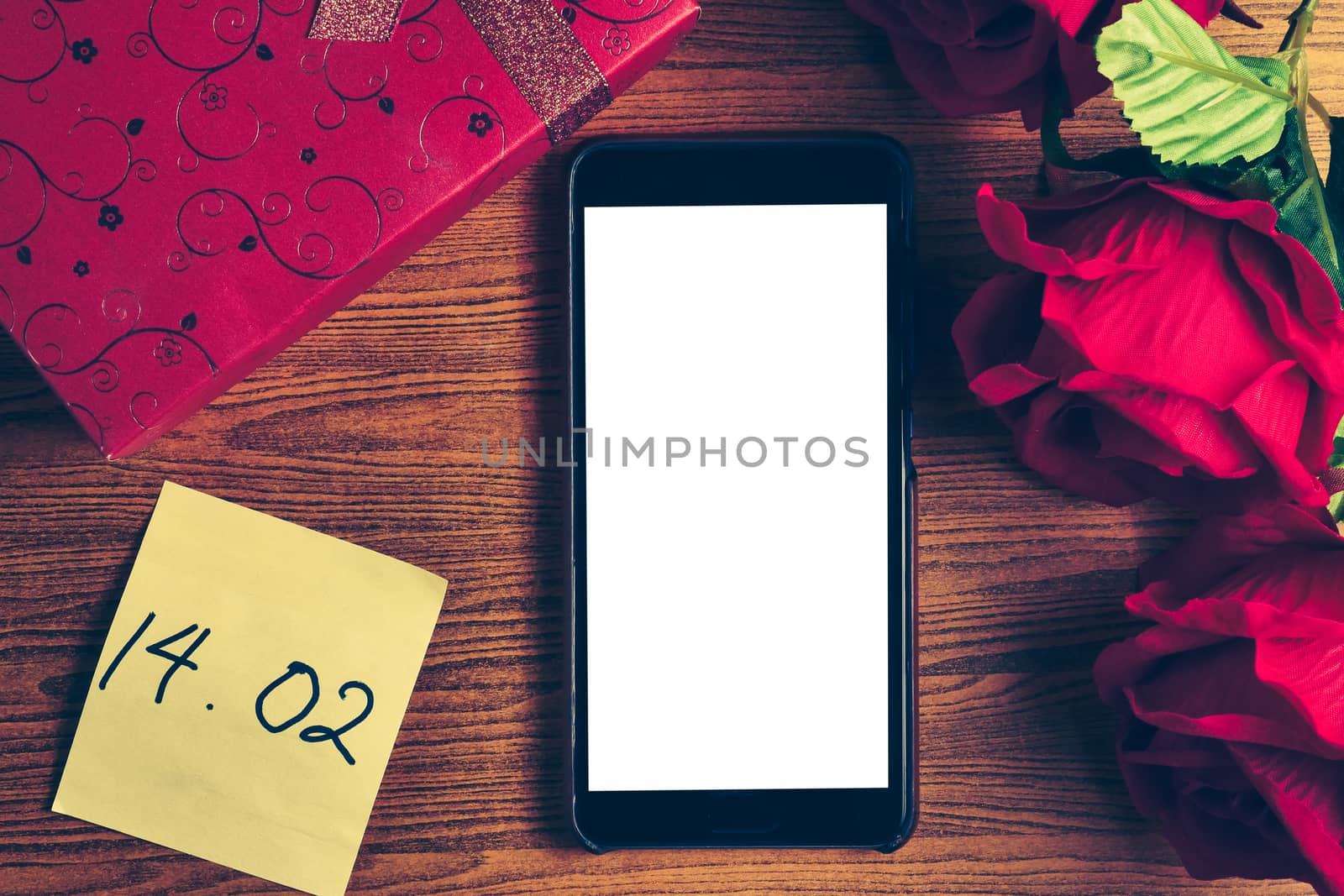 Smart phone with blank screen, gift box and red roses on wooden table. Concept of Valentine Day.