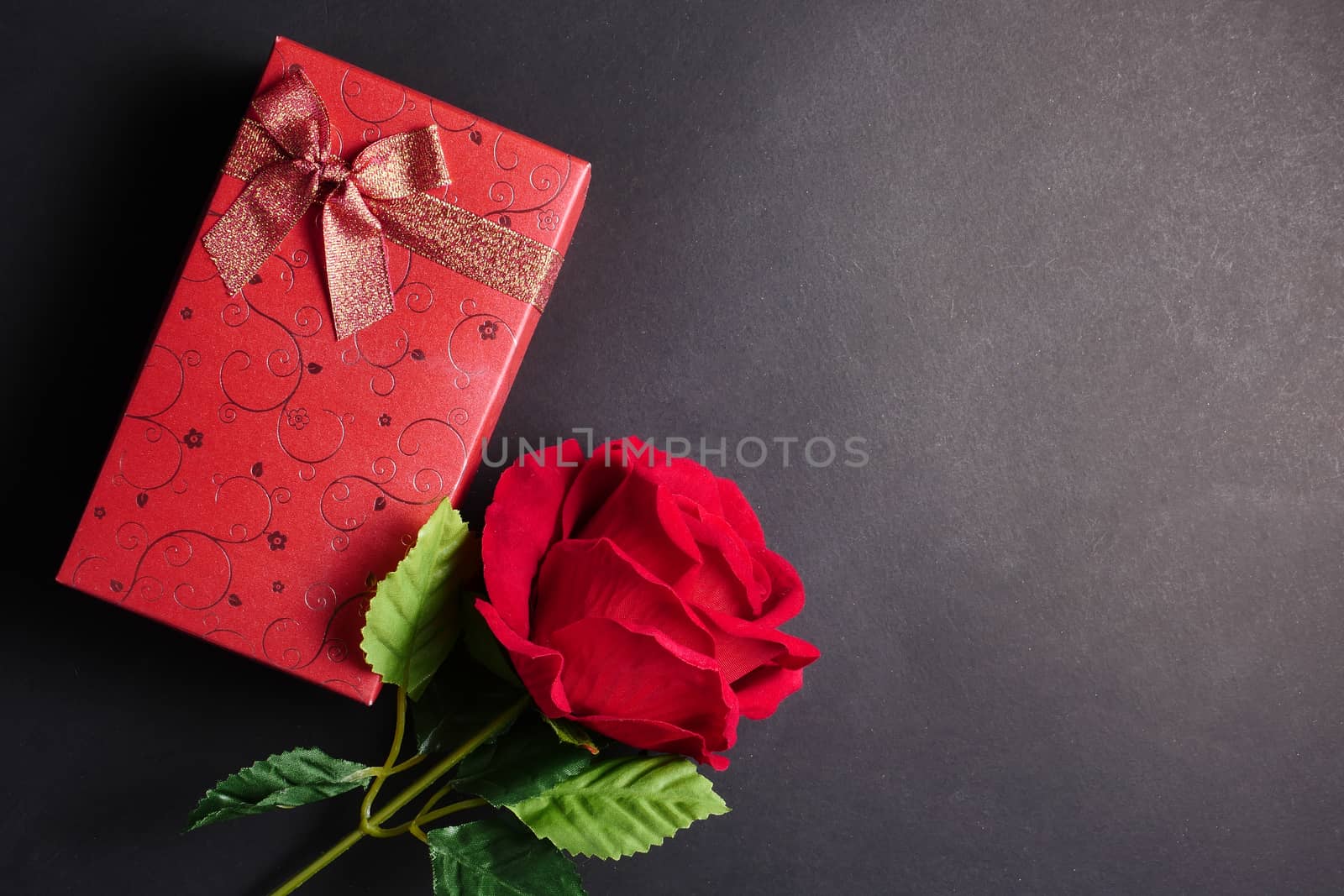 Red rose with red gift box on black background. Free space for text. Concept of Valentine Day.