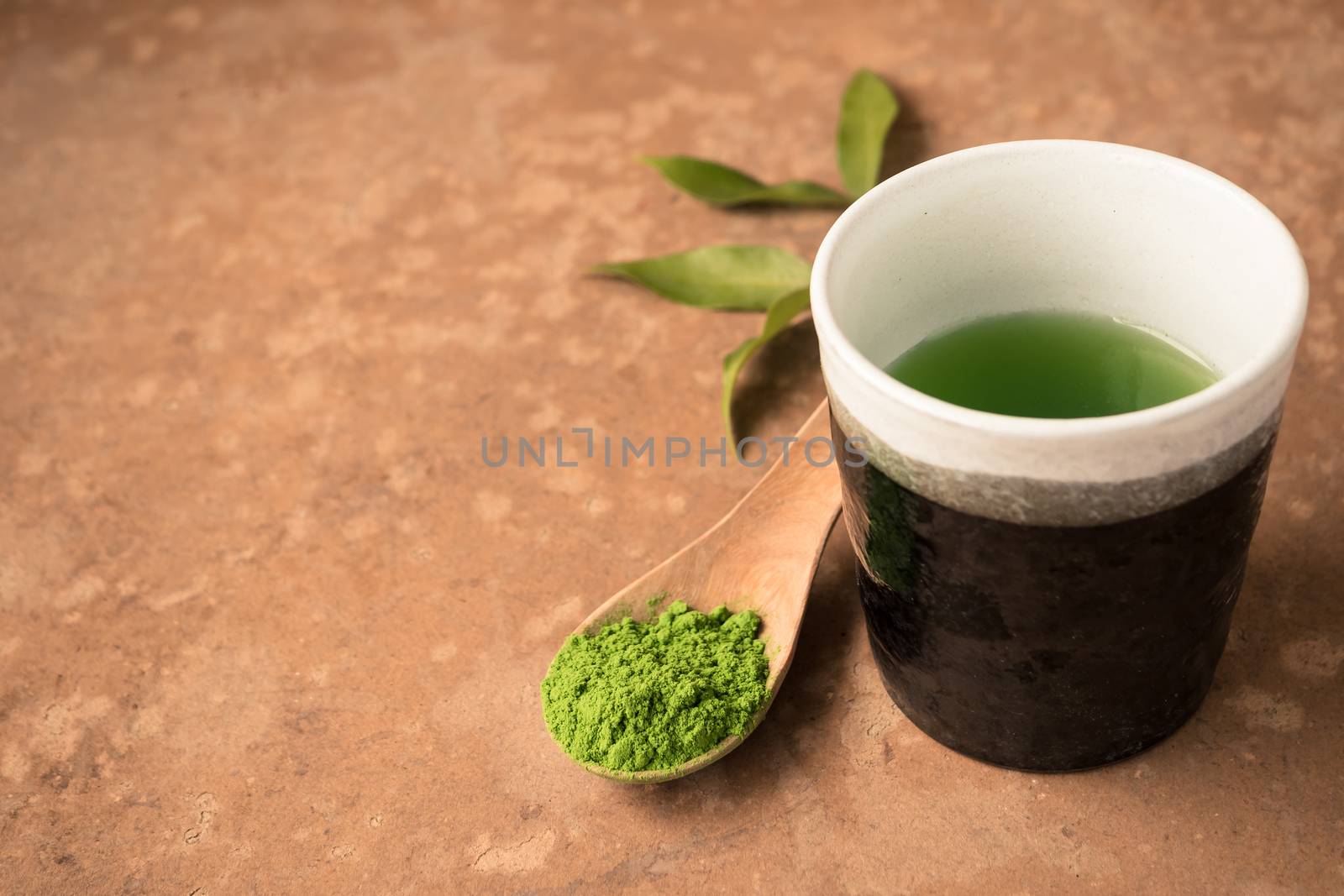 Cup of tea with green tea powder in wooden spoon on the table. Free space for text