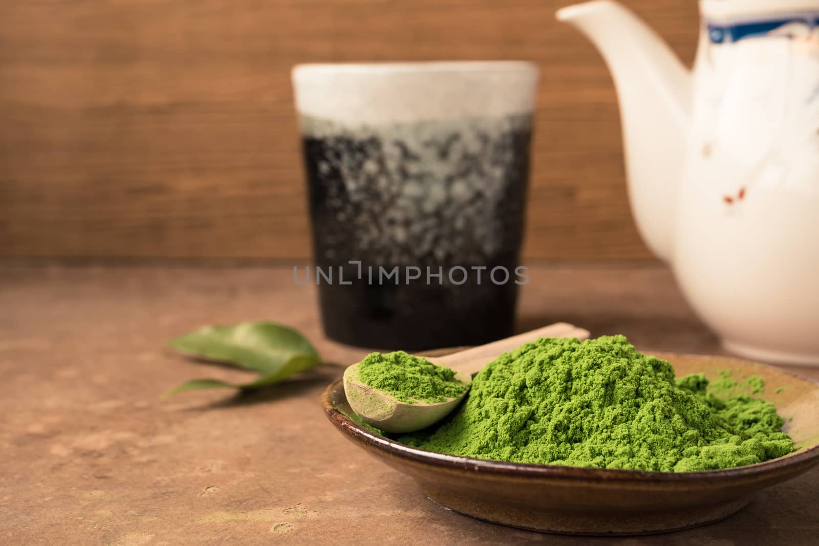 Close up of green tea powder in dish on the table with ceramic cup and teapot background.