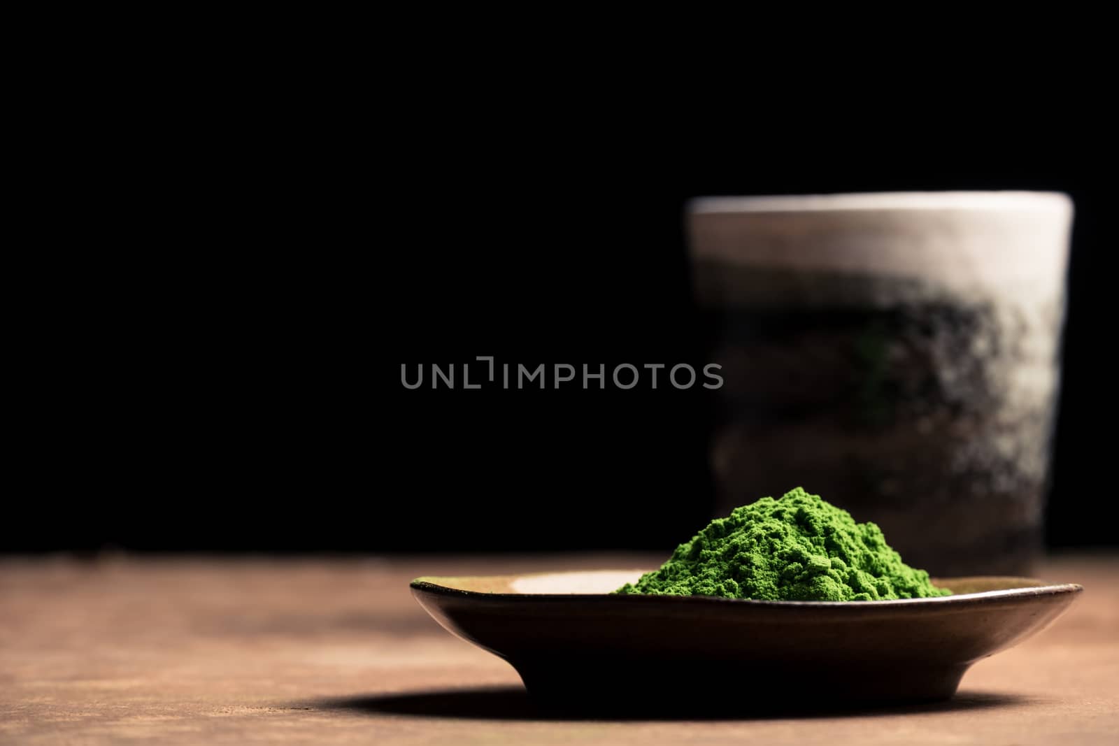 Green tea powder with ceramic cup on the table, black background by ronnarong