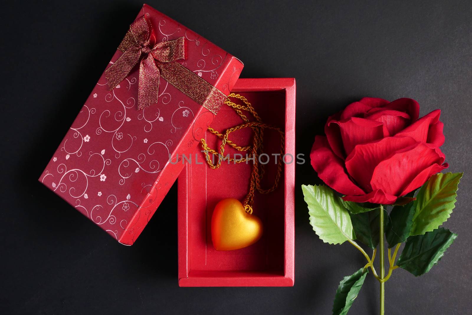 Red rose with gold heart necklace in red gift box on black backg by ronnarong