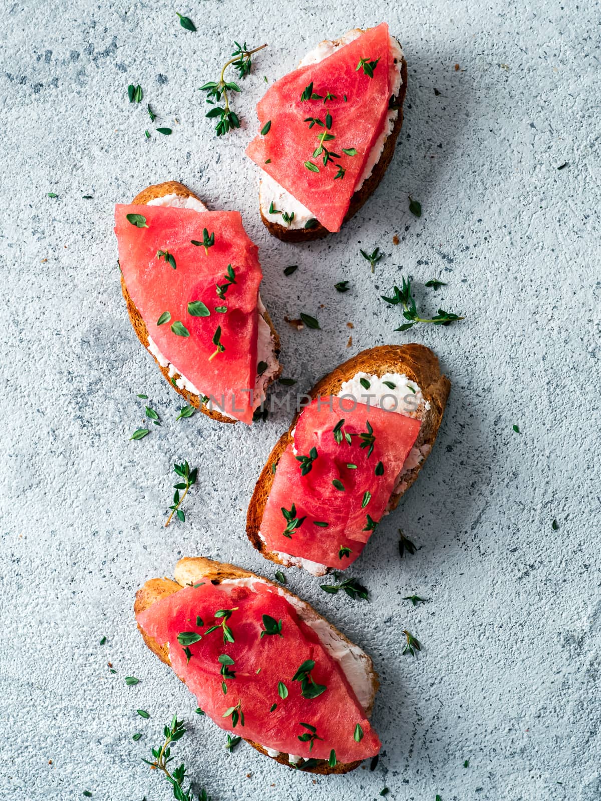 Toasts with soft cheese and watermelon.Salty cheese,sweet watermelon and spicy thyme on crispy grilled bread slices.Idea and recipe for unusual healthy breakfast,summer snack or lunch.Top view flatlay