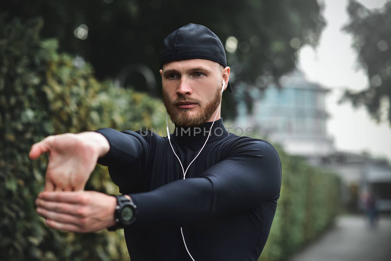 Muscular sportsman stretching out before a sports training at the street in city park