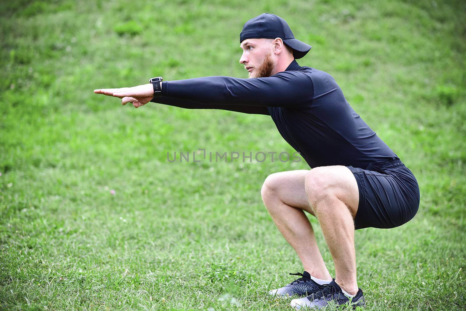 Full length of young concentrated sportsman doing squats outdoors.
