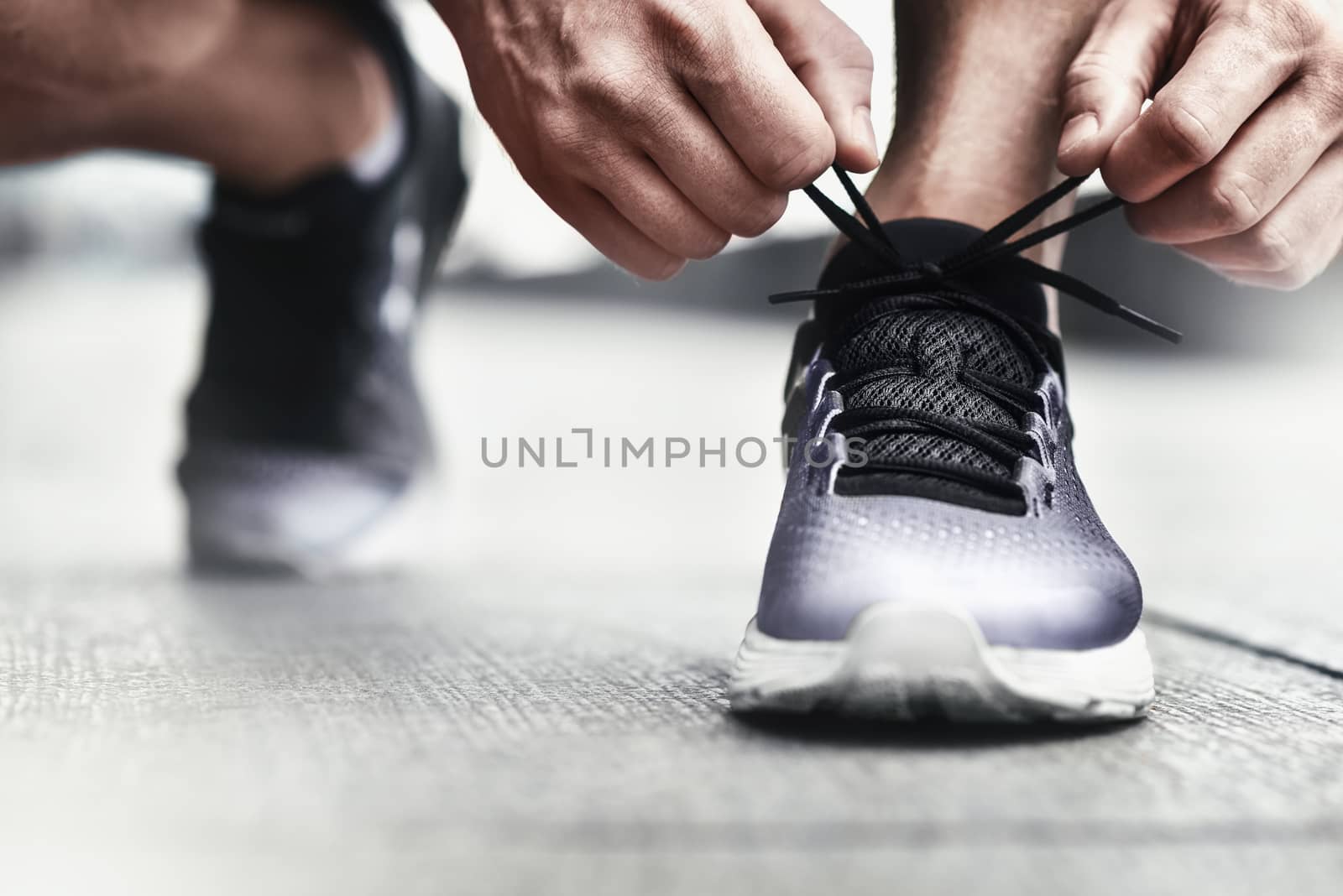 Cropped image of hands tying shoelaces on sneaker, running surface background. Hands of sportsman with pedometer tying shoelaces on sporty sneaker. Running equipment concept. Shoelaces tying by male hands.