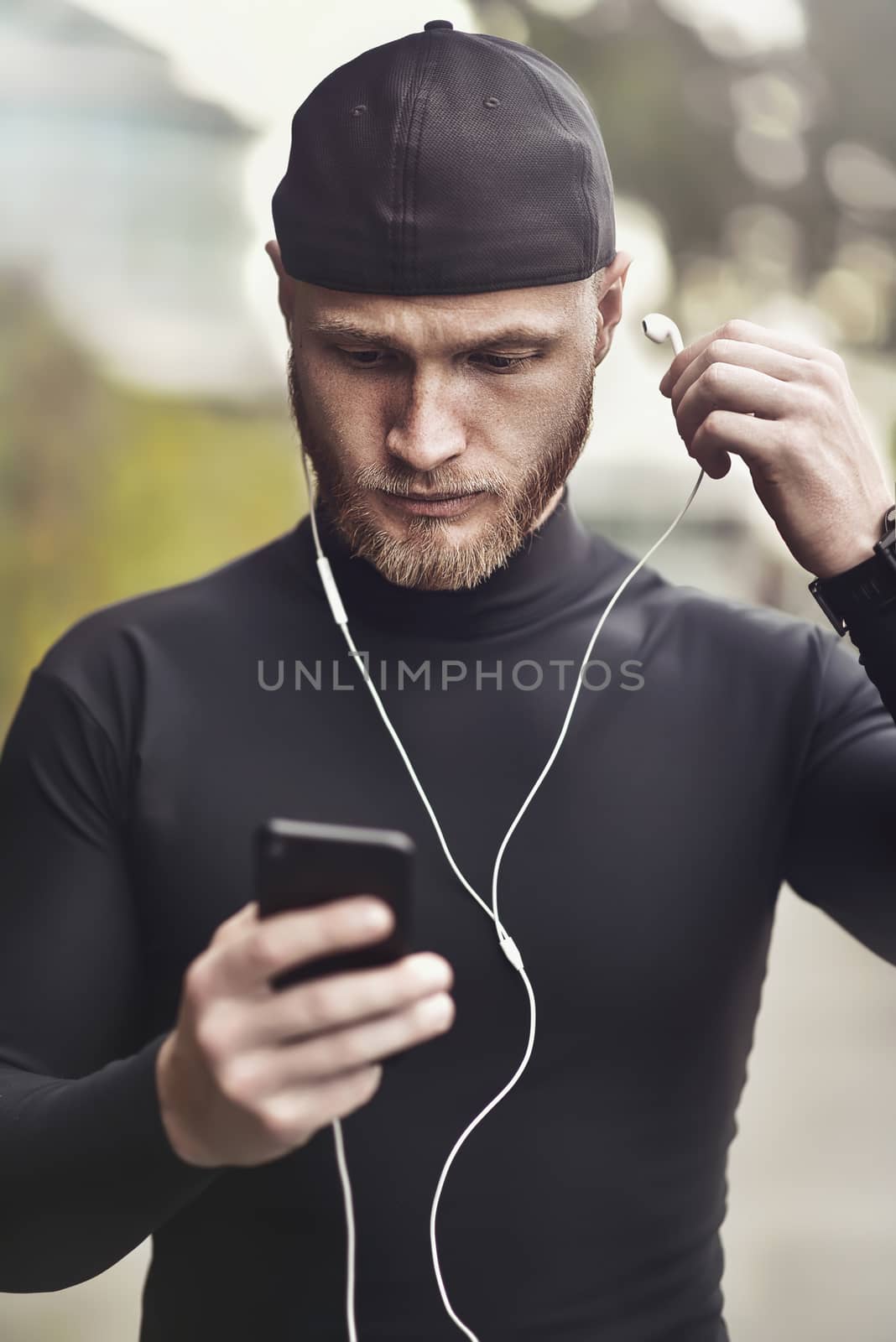 Close-up shot of young white man with beard putting headphone in his ear. Determined sportsman is ready for long-distance run and workout Athlete wearing sport fitness tracker and headphones.