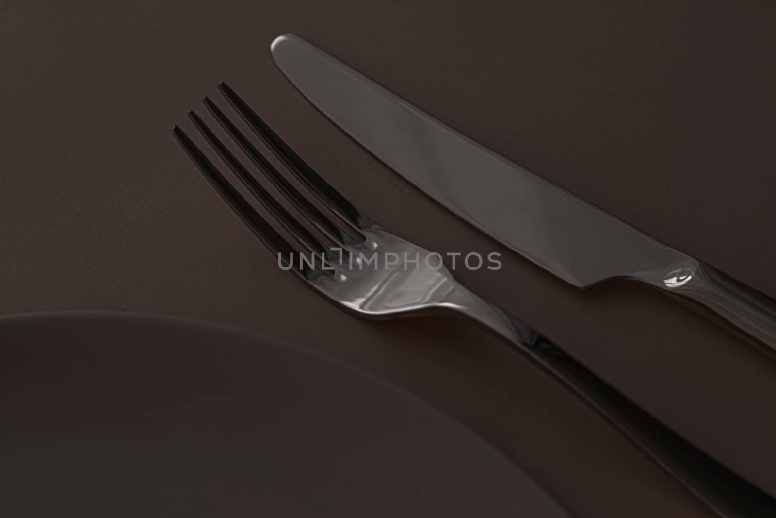 Empty plate and cutlery as mockup set on dark brown background, top tableware for chef table decor and menu branding by Anneleven