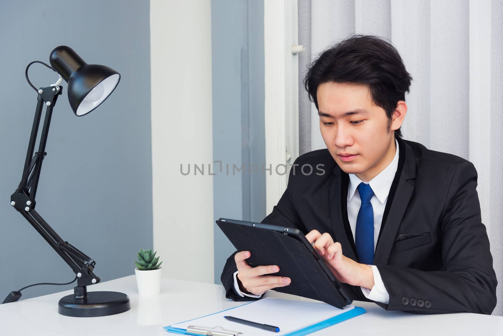 Work from home, Asian young businessman video conference call or facetime he smiling looking to tablet sitting on desk using smart digital tablet computer touching on screen at home office