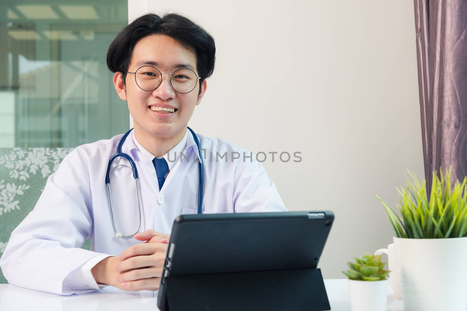 Happy Asian young doctor handsome man smile wear glasses use modern smart digital tablet computer sit and listen patient explain symptoms on desk at hospital office, Technology Healthcare And Medicine