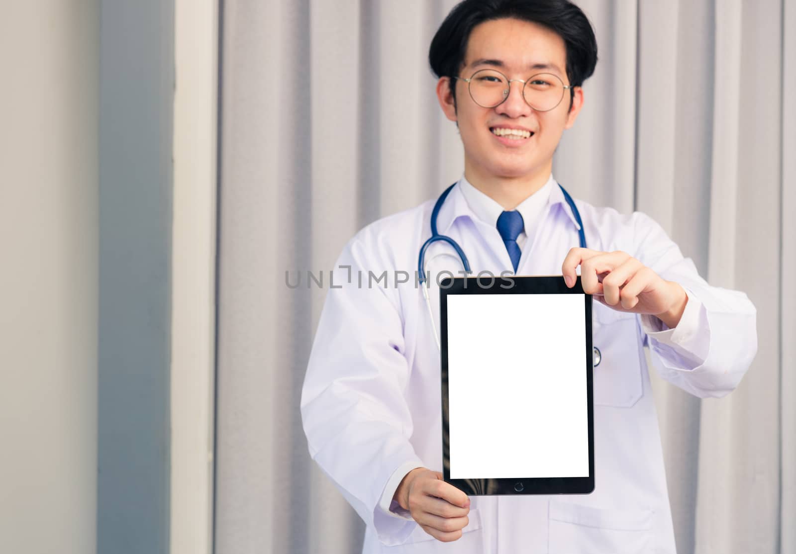 Portrait closeup of Happy Asian young doctor handsome man smiling in uniform and stethoscope neck strap showing front blank screen smart digital tablet on hand, Healthcare medicine concept
