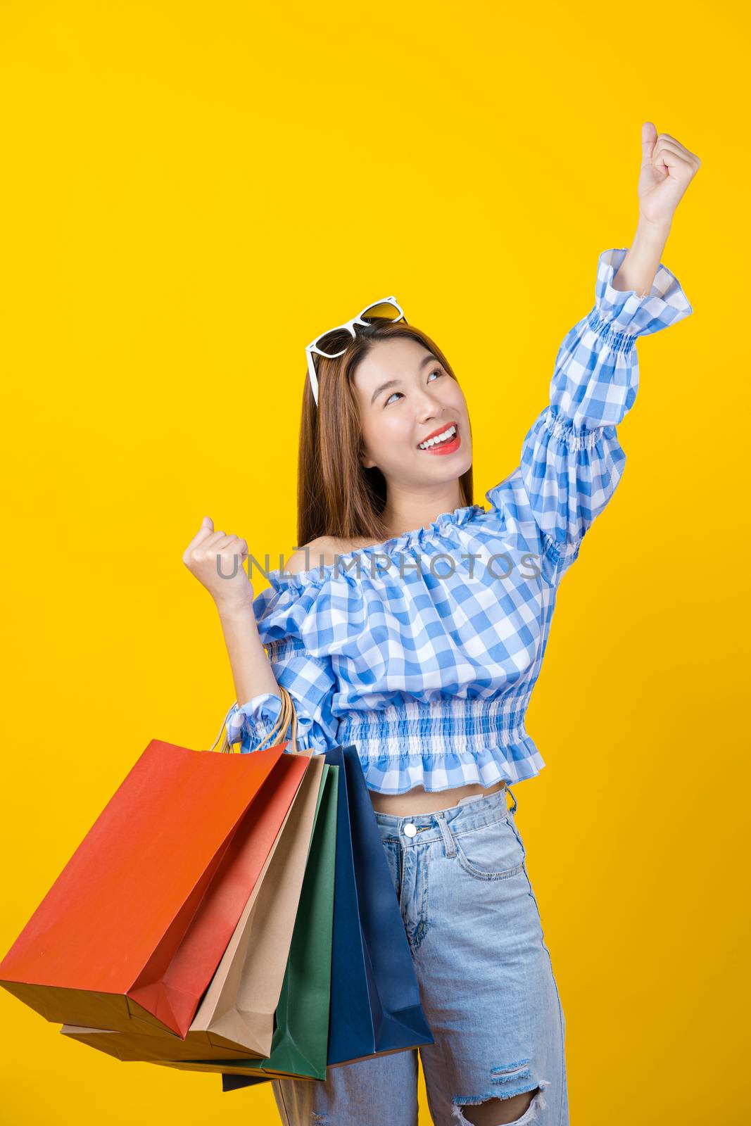 Attractive Asian smiling young woman Carrying shopping coloful bag on isolated yellow color background, copy space and studio, black friday season sale concept.