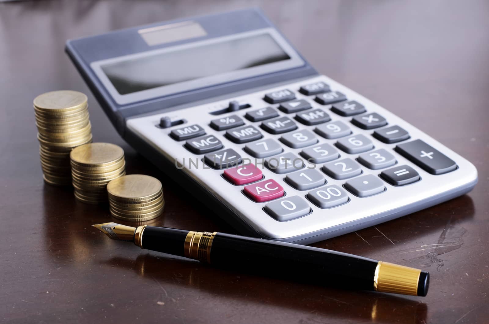 Fountain pen and calculator and coins stack on wooden table for loan money concept