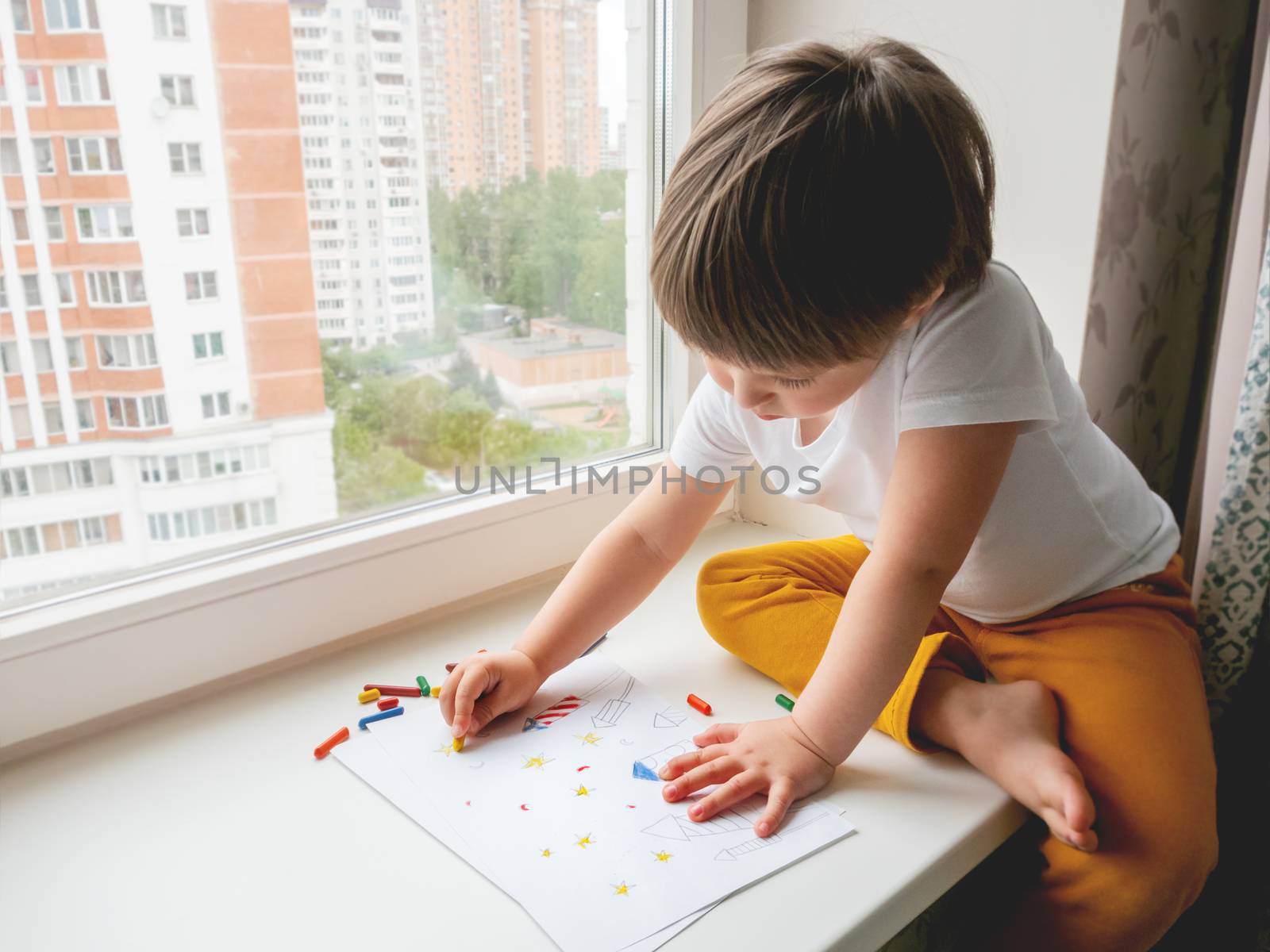 Toddler sits on windowsill and paints colorful fireworks. Child's picture to 4th of July celebration. Independence Day of USA symbol.