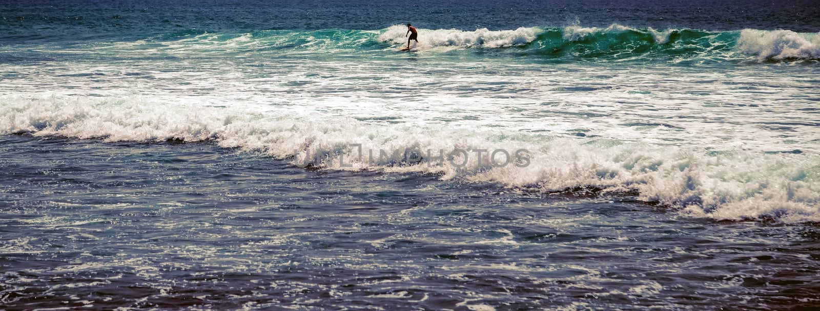 Surfer man on Blue Ocean Wave Bali Indonesia water sport lessons swimming activity riding waves