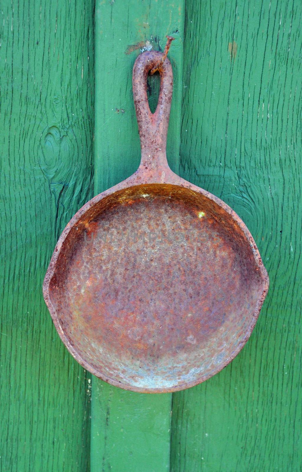Old rusty frying pan hanging on green wall of cabin