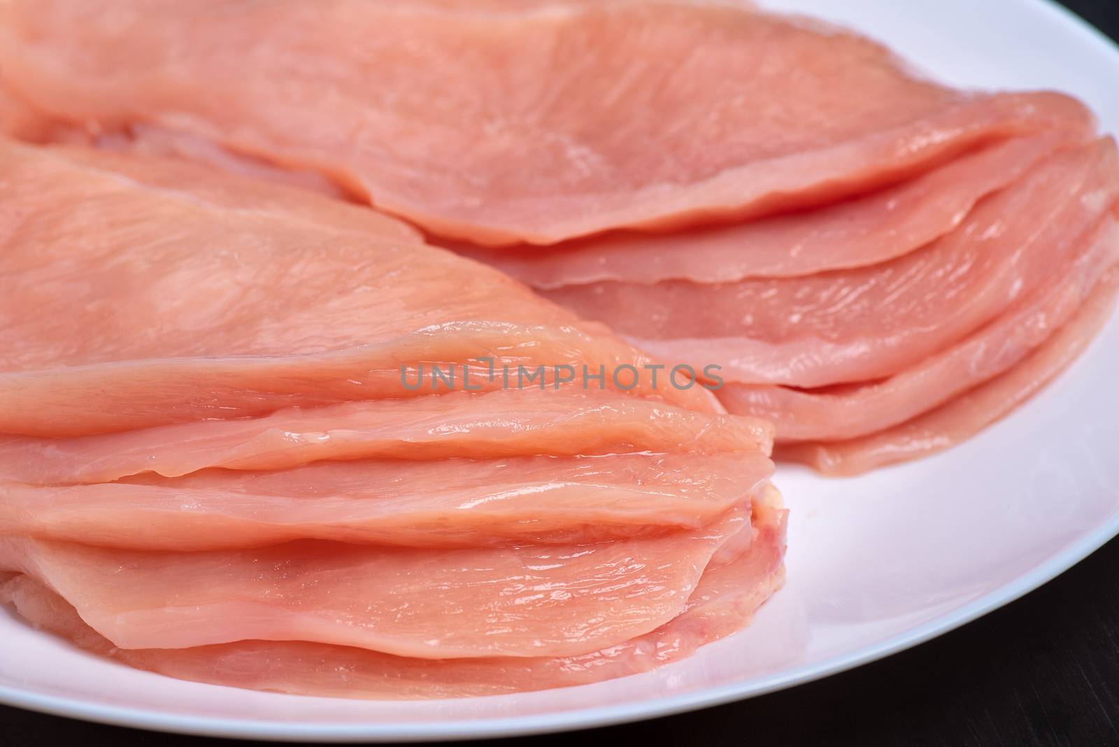 Raw sliced chicken meat close-up on a white plate and on a white background. Satilisimo. Culinary. Top view.Delicious dietary meat.