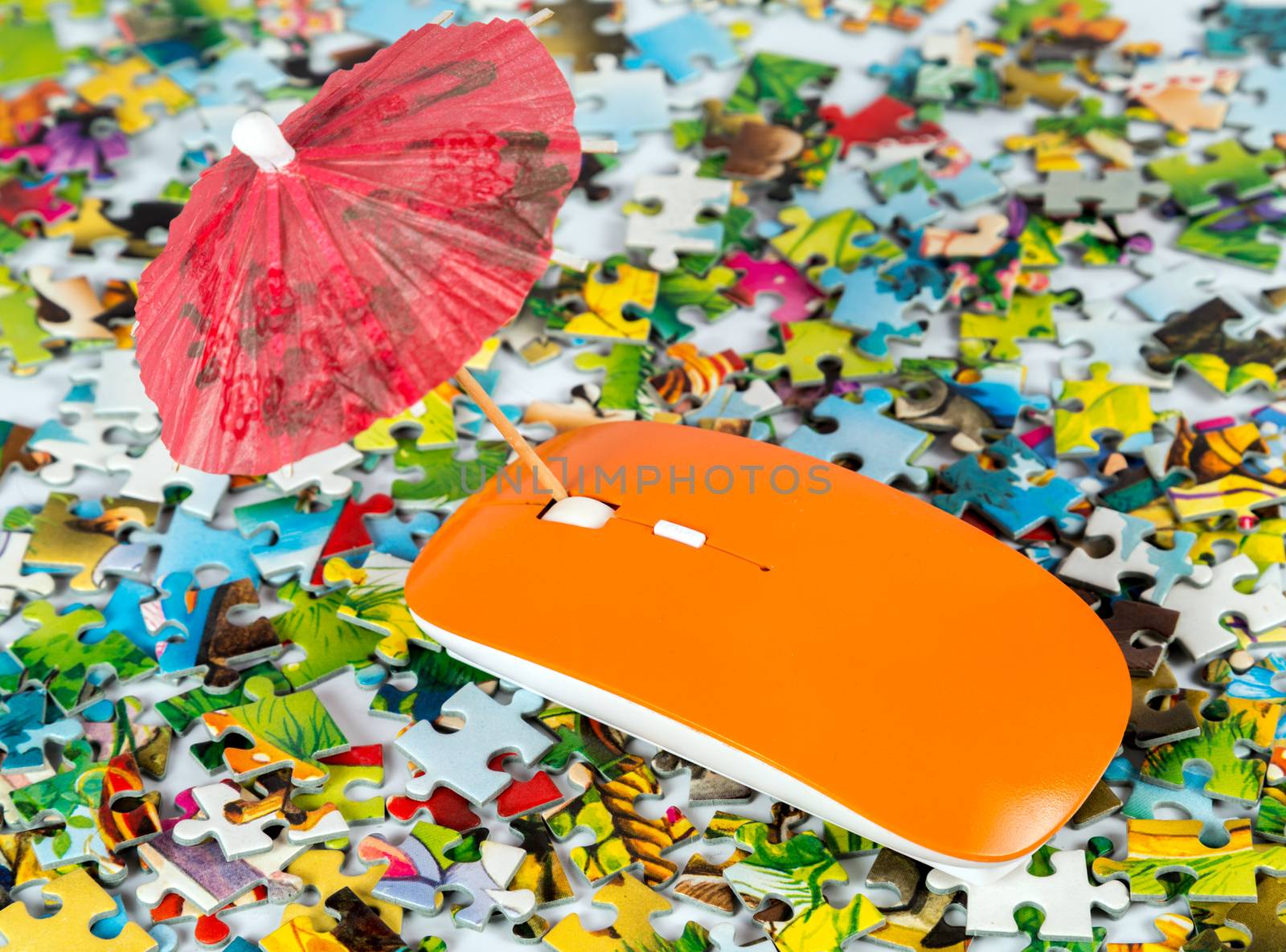 orange computer mouse with umbrella on the puzzle colored pieces background - concept trips tourist